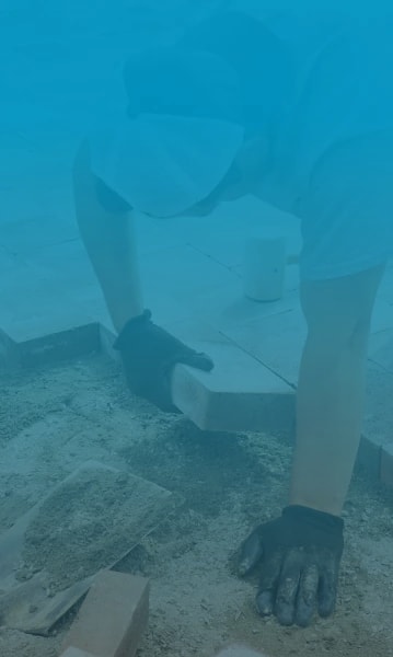 Expert patio installer with gloves on, laying paver bricks on large patio